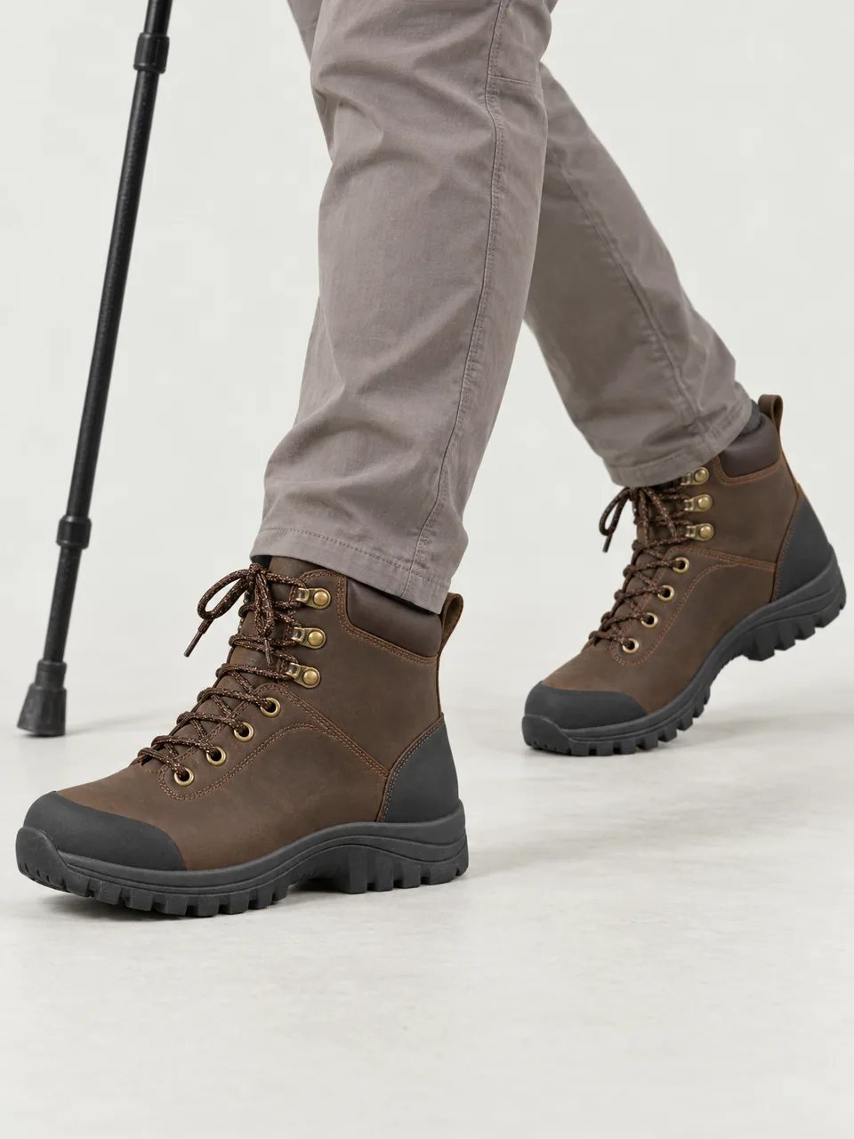 Woman in her 60s, white, slim, short grey hair, walking a chalk downland path with one pole, framed from the knee down wearing the Hale Women's Brae Leather Walking Boot in Peat