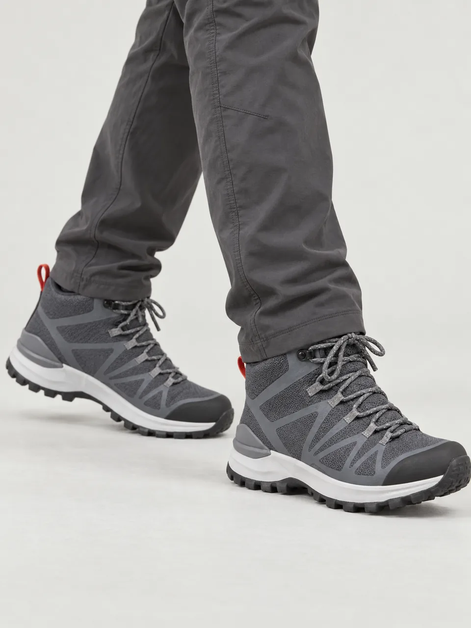 Man in his 30s, South Asian, stocky build, carrying a large pack on a stony hill path, framed from the knee down wearing the Swift Men's Greenshank 410 Lightweight Walking Boot in Slate