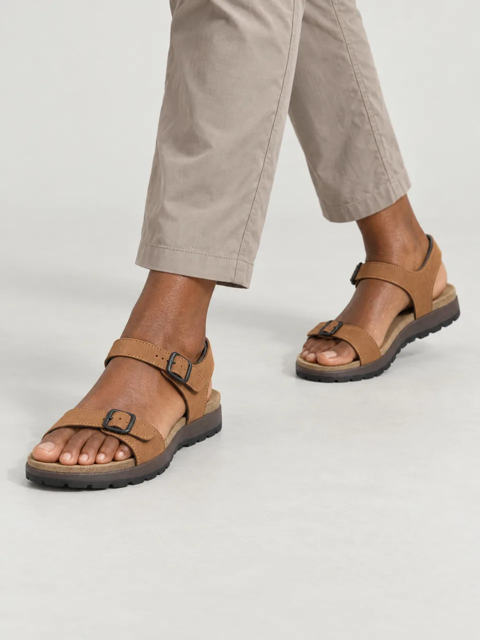 Woman in her 40s, Black British, tall, walking a dry coastal path in a summer dress, framed from mid-calf down wearing the Wayfell Women's Stake Leather Walking Sandal in Tan