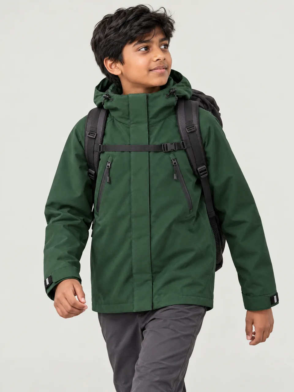 Boy about 12, South Asian, walking uphill on a rocky path with a daypack, hood down, side-front view wearing the Hale Kids' Rigg 3L Waterproof Jacket in Holloway