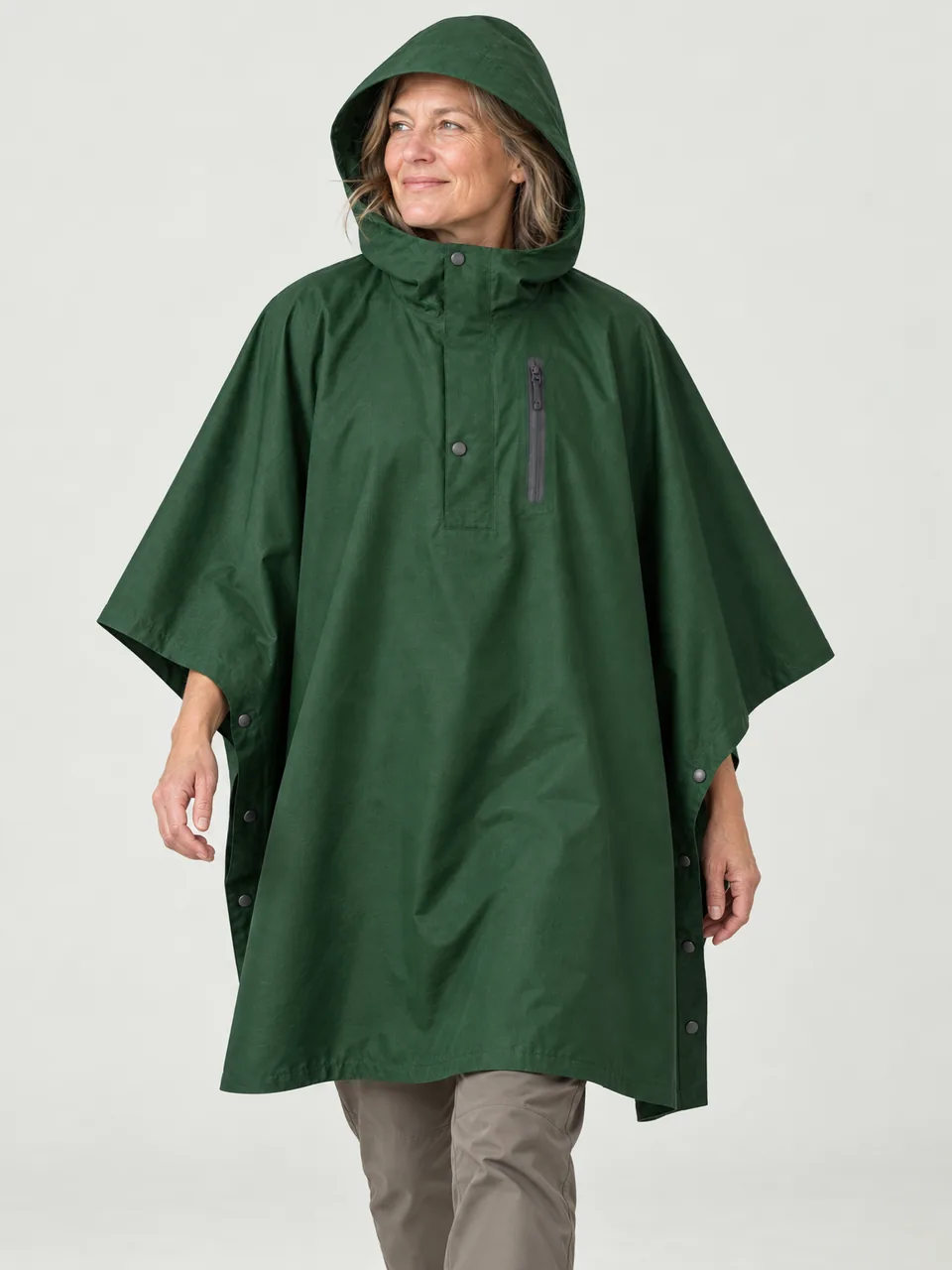 White woman in her 50s, walking a farm track with a daypack under the poncho, hood up wearing the Hale Yett 2L Waterproof Poncho in Holloway