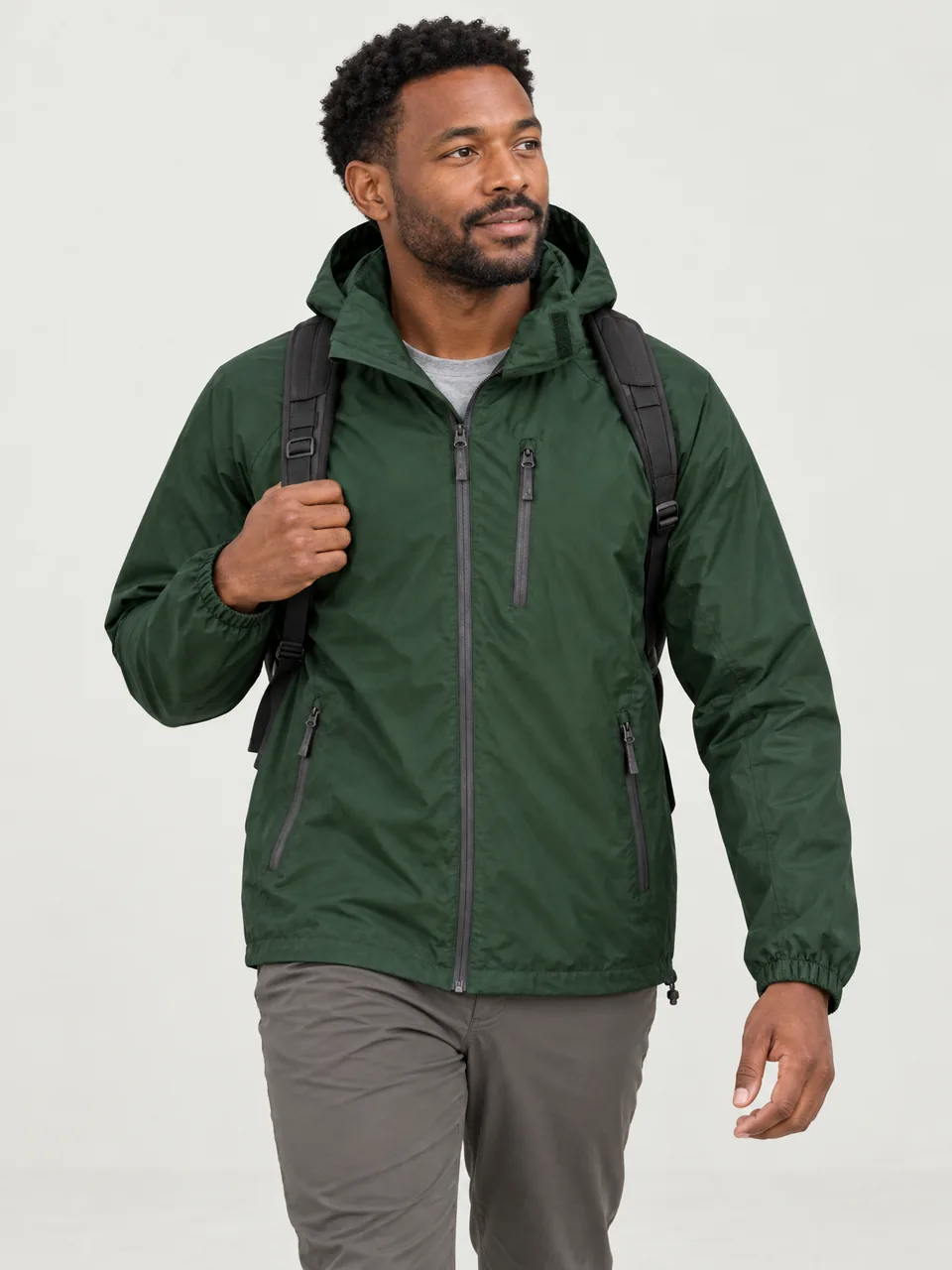 Black man in his 30s, mid-stride on a limestone path, jacket over a T-shirt, small daypack wearing the Hale Men's Intake 2.5L Packable Waterproof Jacket in Holloway