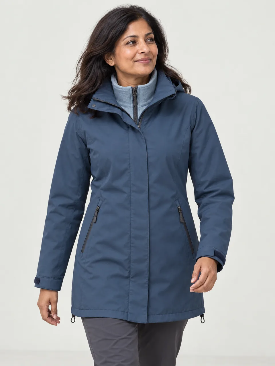 South Asian woman in her 40s, walking beside a dry stone wall, shell and fleece worn together, hood down wearing the Hale Women's Holme 2L 3-in-1 Waterproof Jacket in Tarn