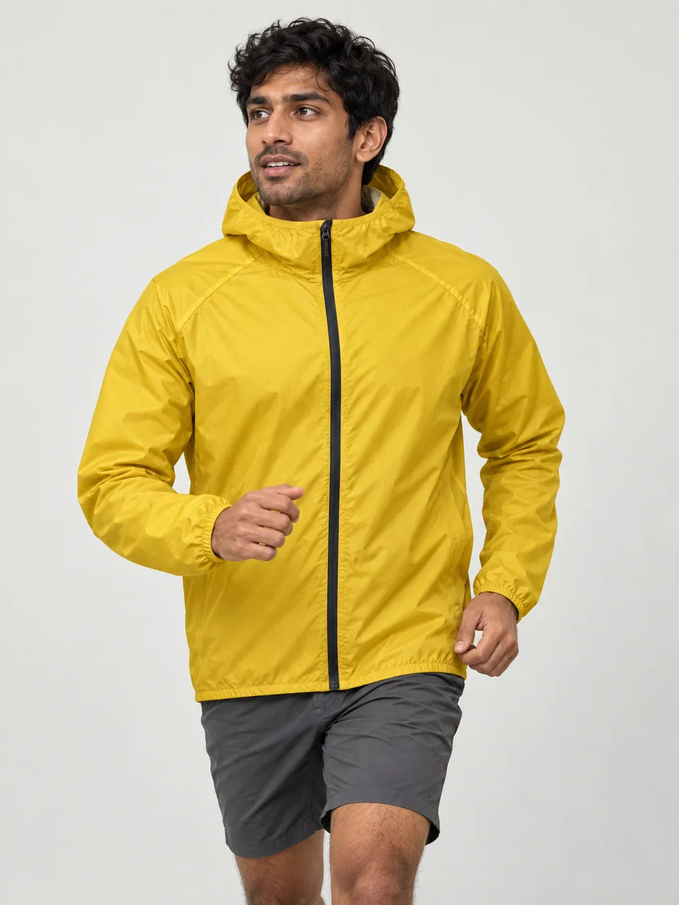 South Asian man in his 20s, lean build, running down a grassy fell path in shorts wearing the Swift Men's Snipe 140 Waterproof Jacket in Gorse