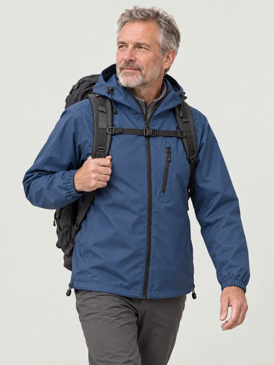 White man in his 50s, grey-haired, walking a high ridge with a 40-litre pack, hood down wearing the Swift Men's Twite 170 Waterproof Jacket in Tarn