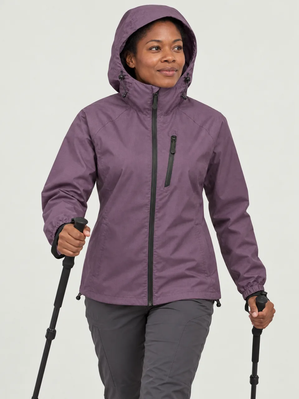 Black woman in her 30s, athletic build, walking fast on a hill path with poles, hood up wearing the Swift Women's Twite 170 Waterproof Jacket in Heather
