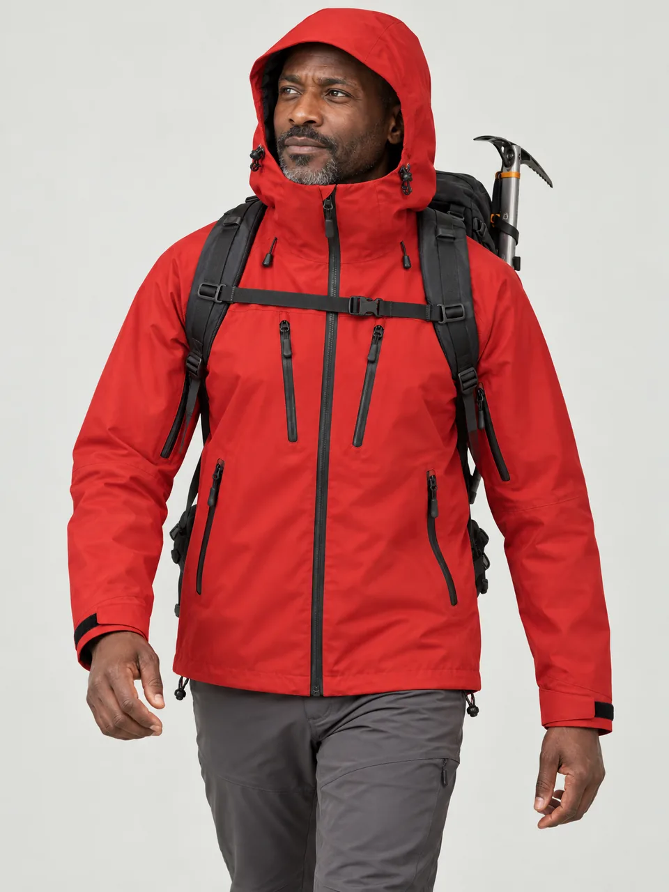 Black man in his 40s, walking a snow-dusted ridge with an ice axe on his pack, hood up wearing the Cairnhope Men's Thole 3L Mountain Jacket in Signal Red