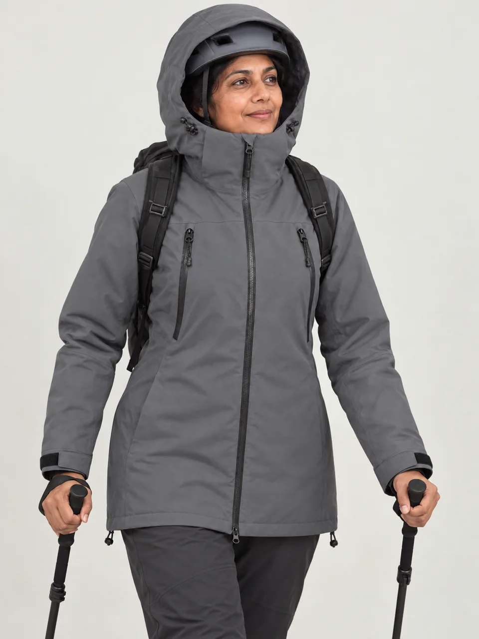 South Asian woman in her 40s, walking a frozen path in low winter light, hood up over a helmet wearing the Cairnhope Women's Blatter 3L Winter Mountain Jacket in Storm Grey