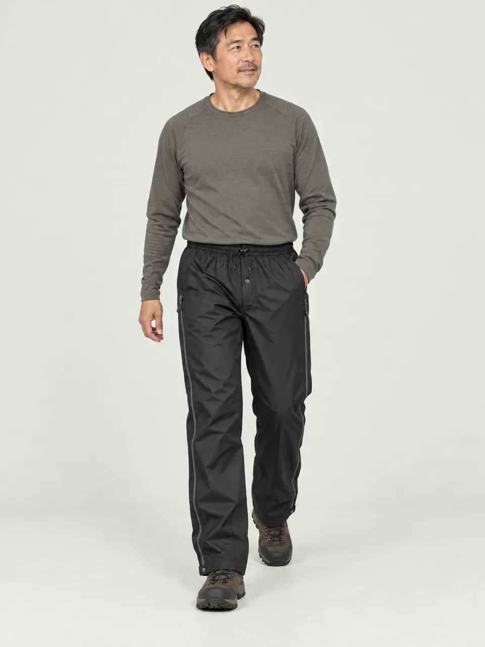 East Asian man in his 40s, walking down a rocky path in rain, overtrousers over boots wearing the Hale Men's Cleugh 2.5L Waterproof Trousers in Soot