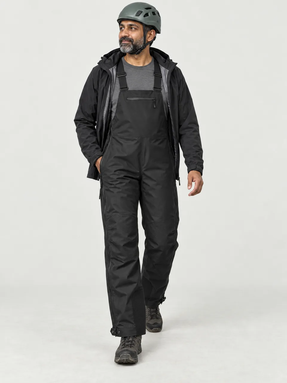 South Asian man in his 40s, walking over wet rock slabs wearing a climbing helmet, bib under an open jacket wearing the Cairnhope Men's Onding 3L Pro Waterproof Bib in Black