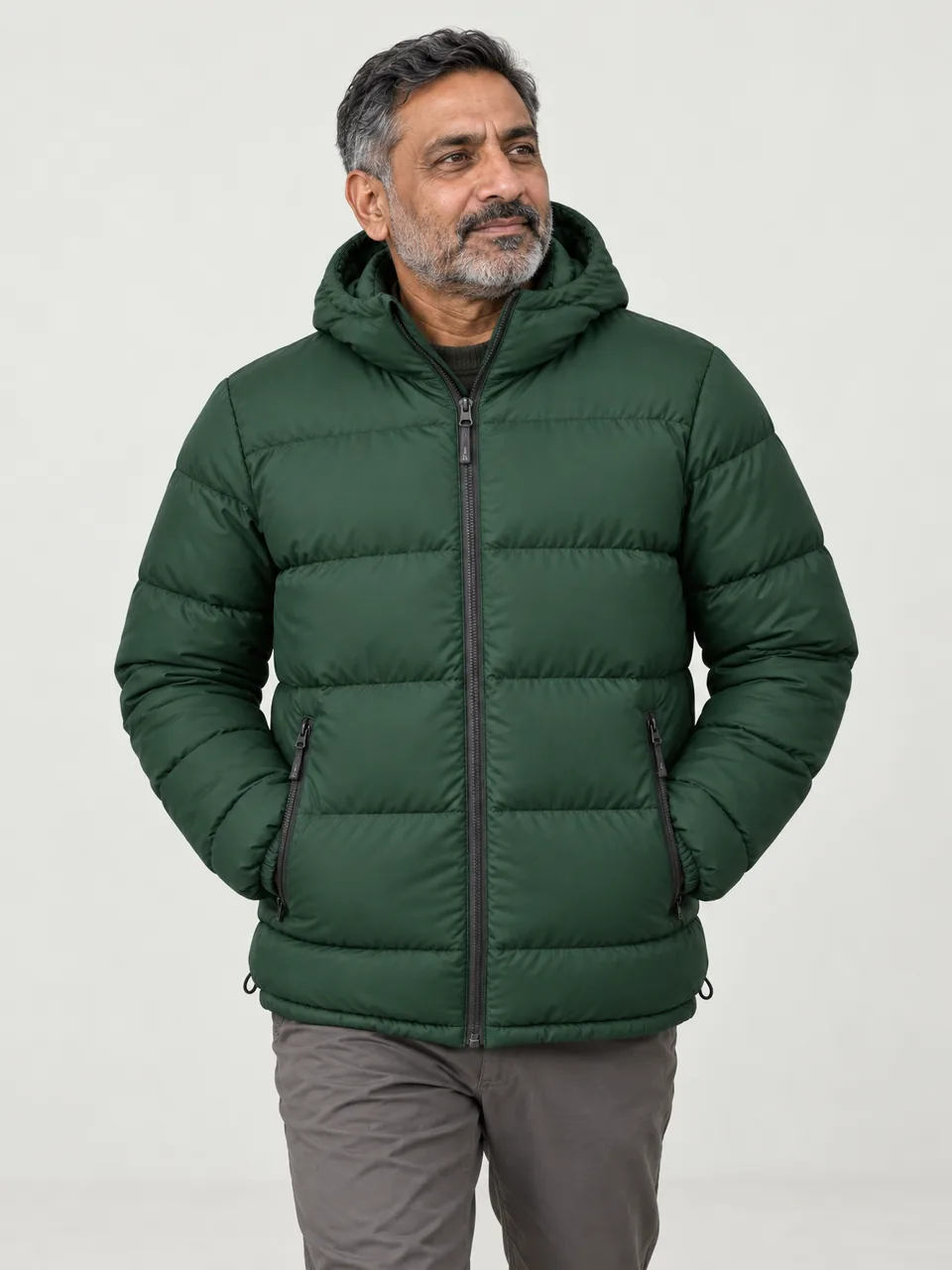 Man in his 50s of Pakistani heritage, walking across moorland in cold light, hood down, hands in pockets wearing the Hale Men's Byre Insulated Jacket in Holloway