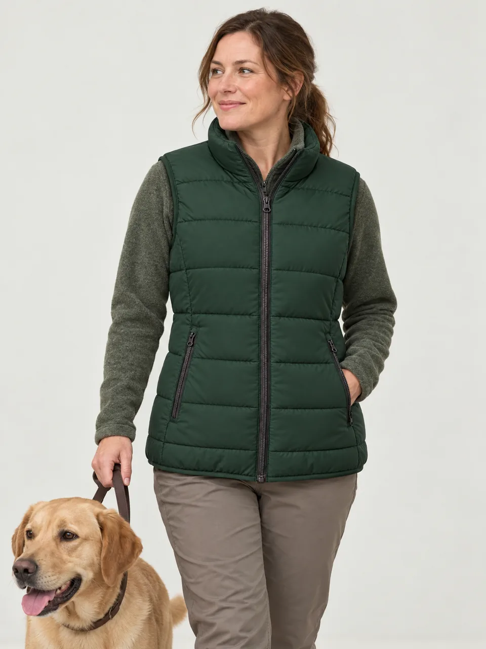 White woman in her 30s, walking a country lane with a dog, gilet over a fleece wearing the Hale Women's Byre Insulated Gilet in Holloway