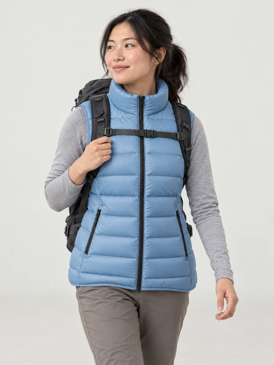 East Asian woman in her 20s, walking a coast path early in the morning with a 35-litre pack, gilet over a long-sleeve top wearing the Swift Women's Wryneck 70 Down Gilet in Sky