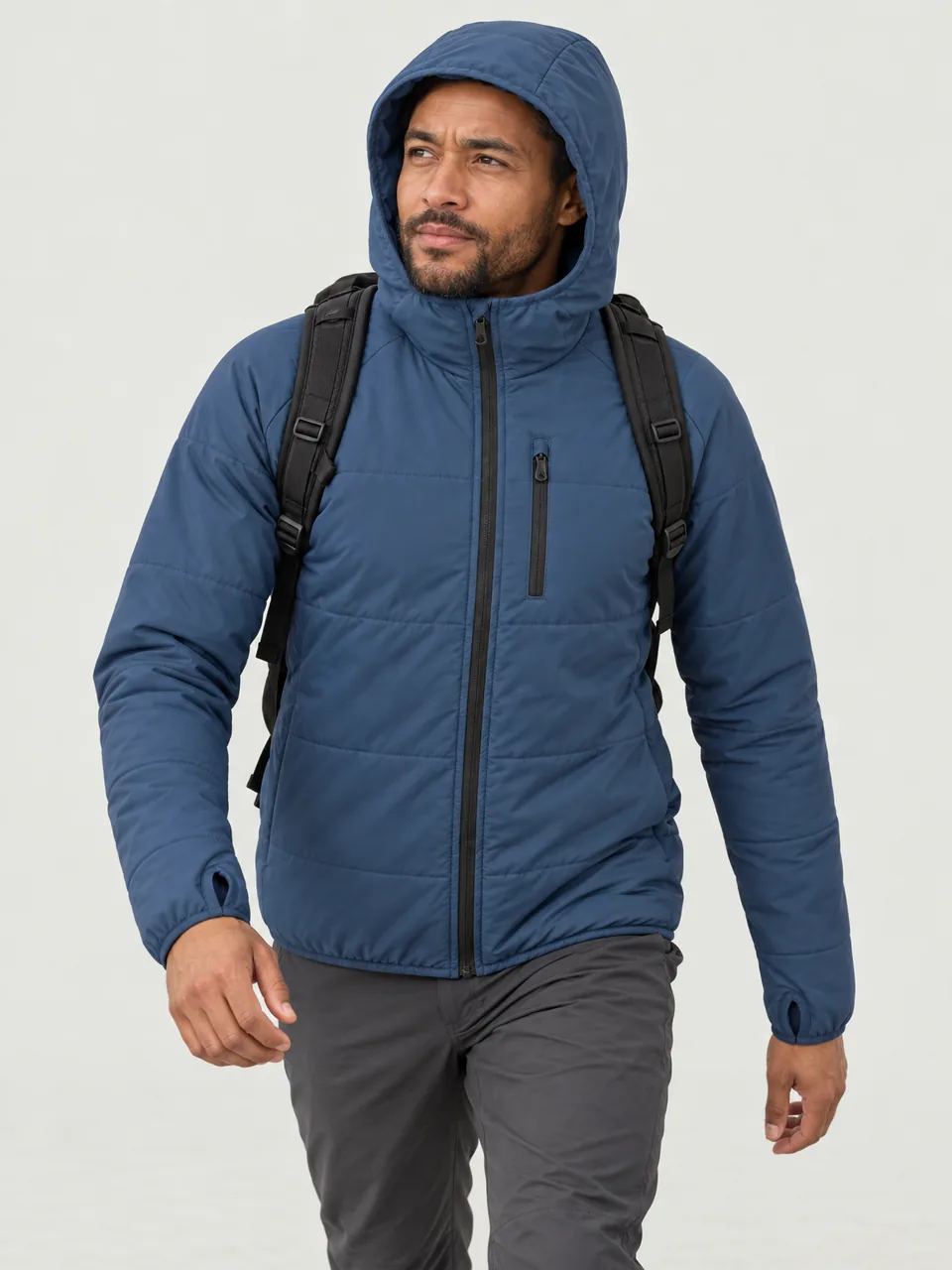 Mixed-race man in his 30s, walking uphill into a cold wind with a small pack, hood up wearing the Swift Men's Dotterel 80 Synthetic Hoody in Tarn