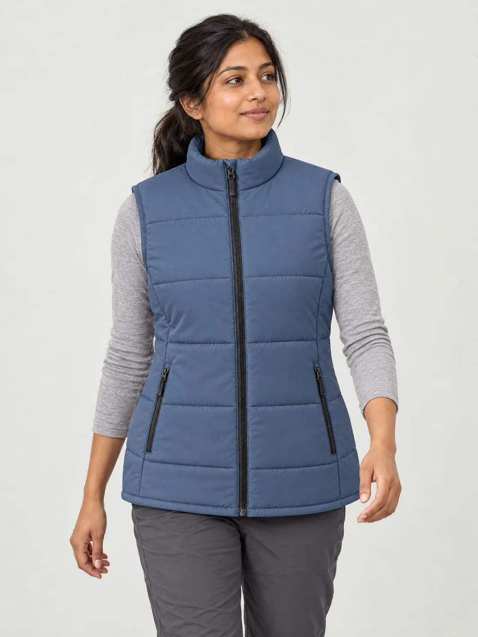 South Asian woman in her 20s, walking a woodland path in autumn, gilet over a long-sleeve top wearing the Northwold Women's Thaw 60 Synthetic Gilet in Dusk Blue