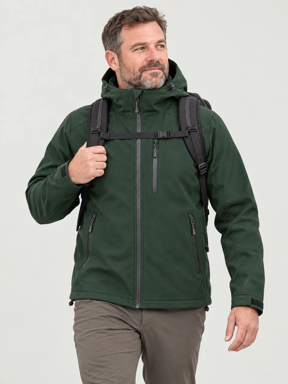 White man in his 40s, stocky build, walking a breezy ridge with a daypack wearing the Hale Men's Laver Softshell Jacket in Holloway