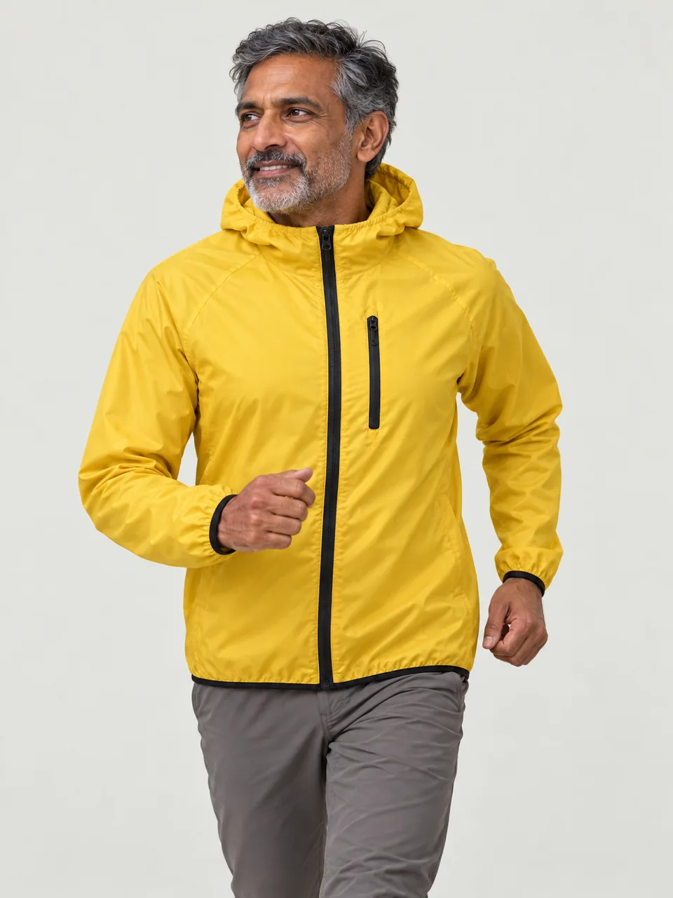 Man in his 50s of Indian heritage, wiry build, running along a high ridge path wearing the Swift Men's Wheatear 75 Windproof Jacket in Gorse