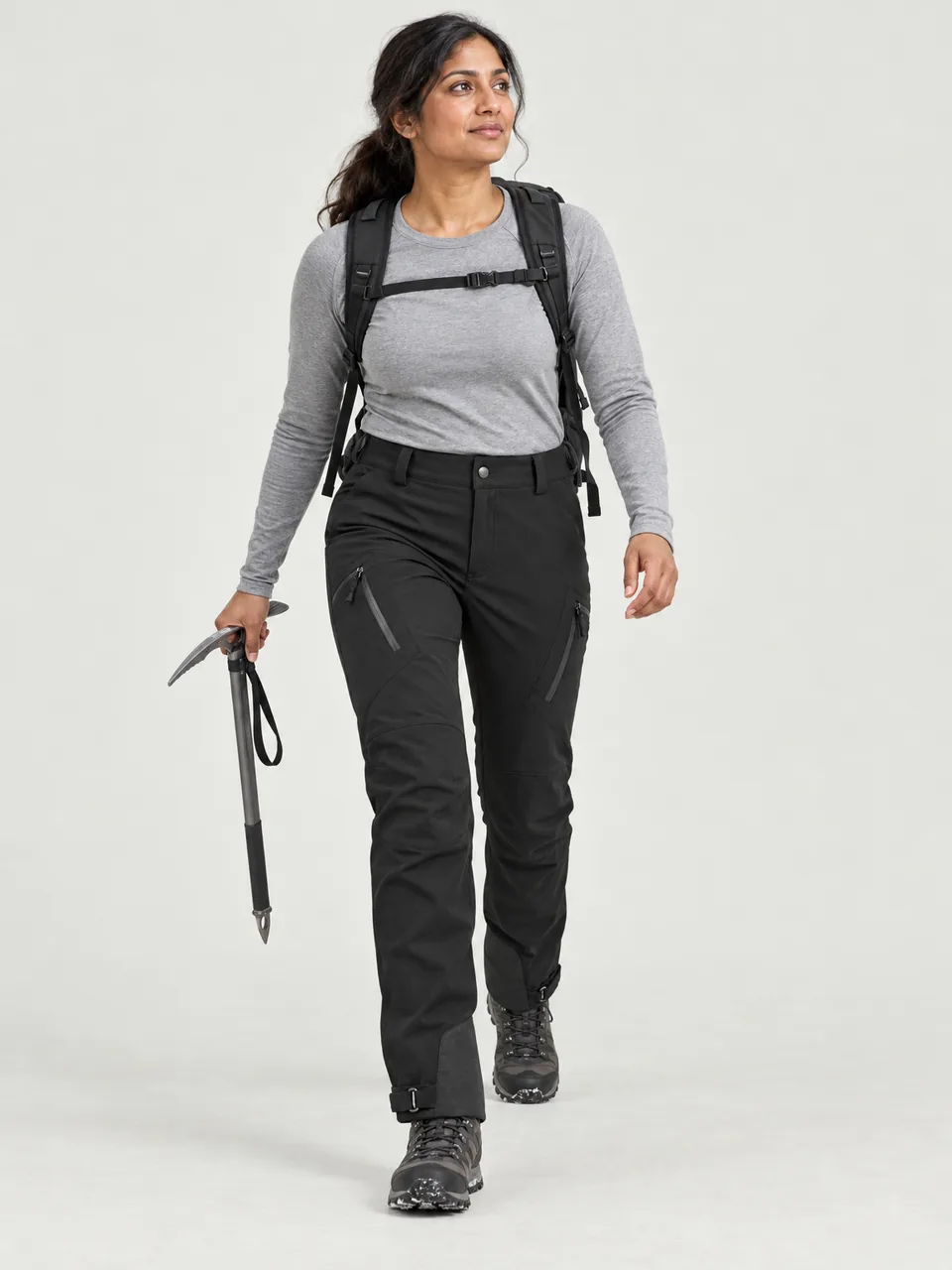 South Asian woman in her 30s, walking up a snowy slope with an ice axe wearing the Cairnhope Women's Haar Softshell Mountain Trousers in Black