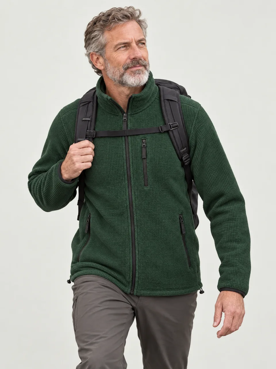 Man in his 50s with a grey beard, walking uphill on a stony fell path with a daypack wearing the Hale Men's Heaf Grid Fleece Jacket in Holloway