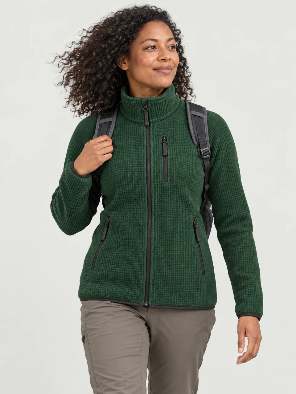 Black British woman in her 30s walking a coast path with a small daypack, wind in her hair wearing the Hale Women's Heaf Grid Fleece Jacket in Holloway