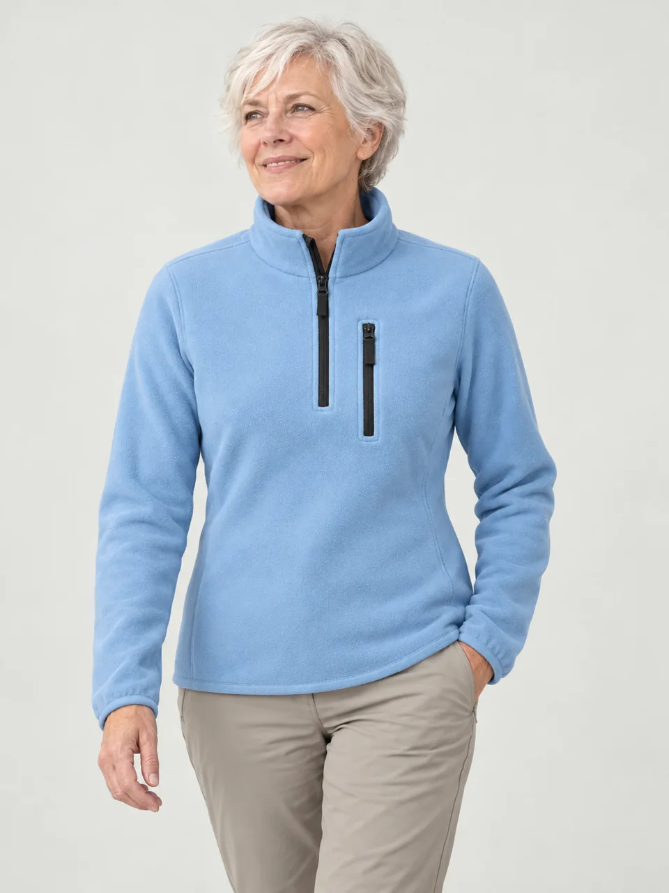 Woman in her 60s with short white hair, walking a lane between stone walls on a bright cold morning wearing the Hale Women's Stell Half-Zip Fleece in Sky