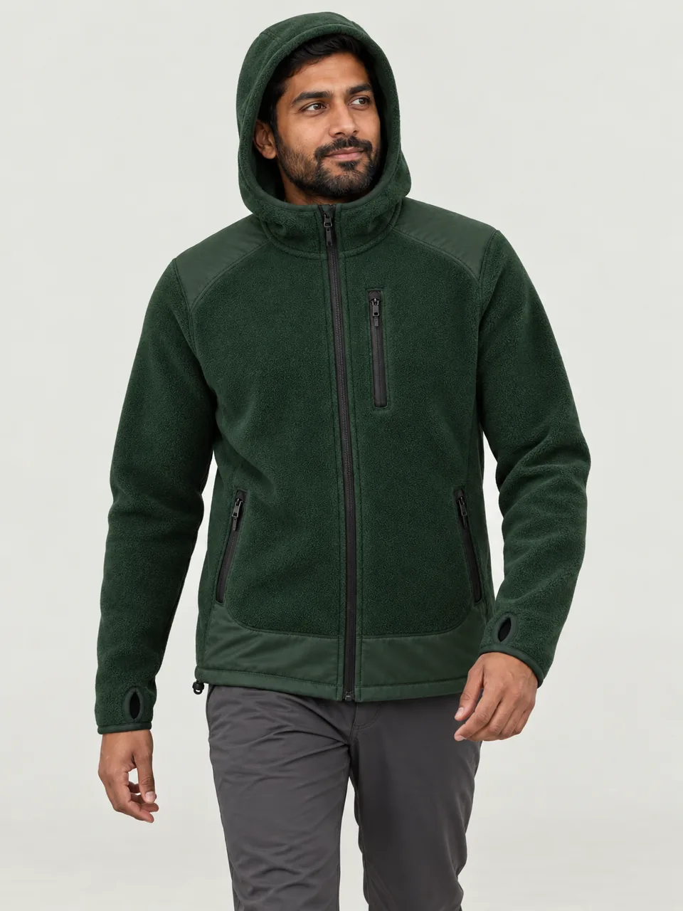Man in his 30s of South Asian heritage, hood up, walking past a pitched tent at dusk wearing the Hale Men's Lownd Hooded Fleece in Holloway