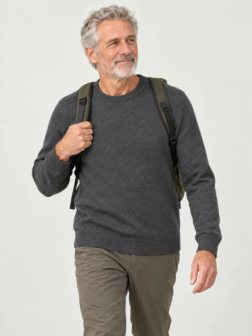 Tall man in his 60s walking through a Dales hay meadow with a small daypack wearing the Greywether Men's Menhir 330 Merino Crew Jumper in Charcoal Marl
