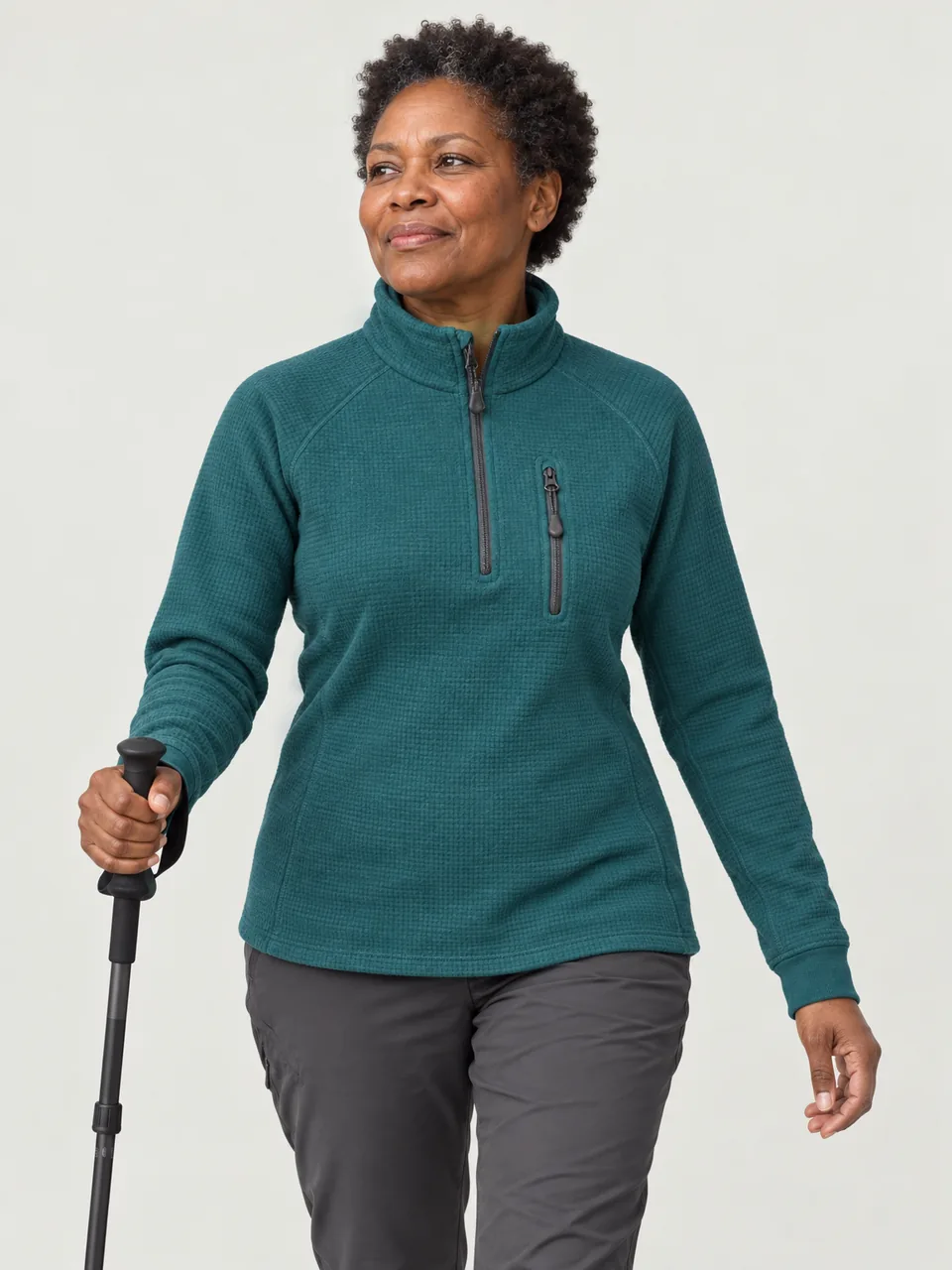 Black woman in her 50s with short natural hair, walking a frosty moor path with one walking pole wearing the Greywether Women's Dolmen 300 Merino Grid Half-Zip in Teal