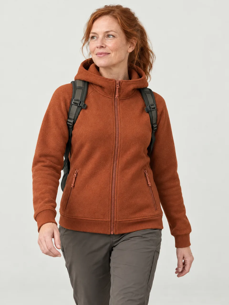 Woman in her 40s with red hair tied back, walking a forest track in Wicklow in autumn with a daypack wearing the Greywether Women's Henge 280 Merino Fleece Hoody in Rust