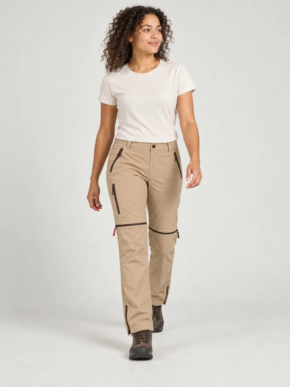 Woman in her 20s of mixed heritage with curly hair, walking a lochside path on a sunny day wearing the Hale Women's Inbye Convertible Trousers in Sandstone