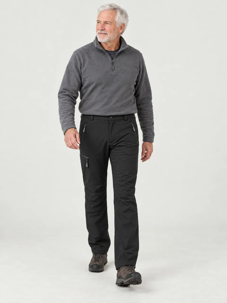White-haired man in his 60s walking through light snow on a moorland track wearing the Hale Men's Hemmel Winter Trousers in Soot