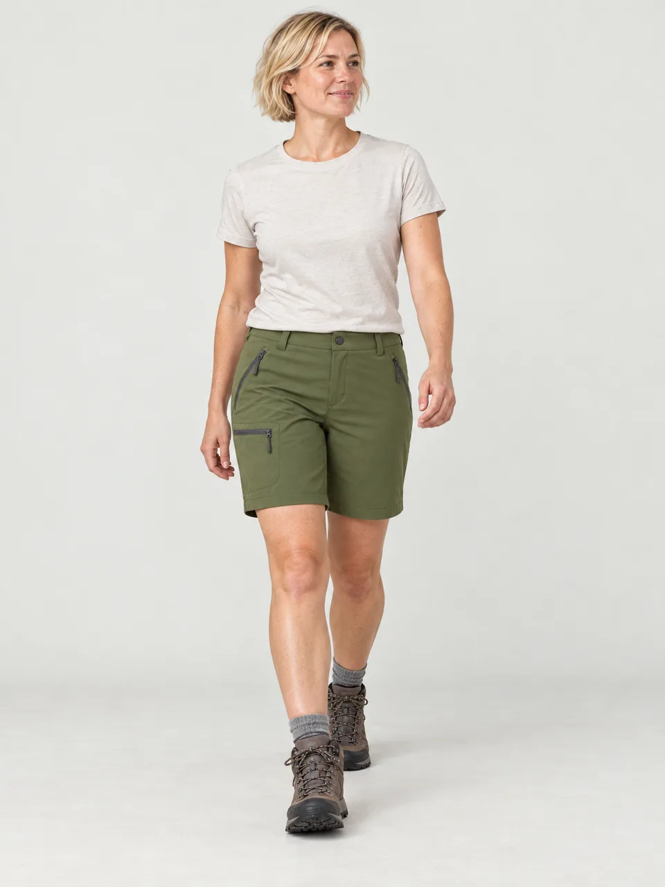 Woman in her 30s with short blonde hair, walking a chalk track on the South Downs in summer wearing the Hale Women's Inbye Walking Shorts in Moss