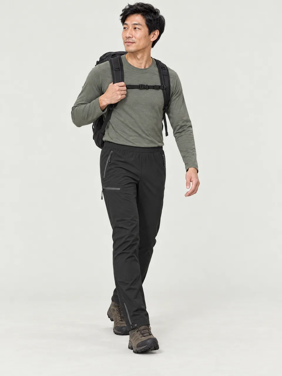 Lean man of Chinese heritage in his 30s, striding up a steep grassy ridge with a light pack wearing the Swift Men's Godwit 260 Trail Trousers in Soot