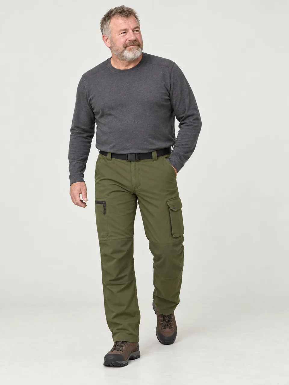 Stocky Scottish man in his 50s crossing stepping stones over a beck on a fell path wearing the Rakefoot Men's Causey Trousers in Olive